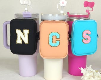 Puede incluir: Tres vasos térmicos con mangas de neopreno de diferentes colores. Las mangas tienen cierre de cremallera y un parche de fieltro con una letra. Las letras son N, C y S. Los vasos son morado, blanco y rosa.