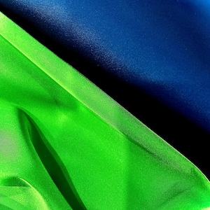 May include: Abstract image featuring a diagonal composition of vibrant colors. A bright green fabric or material is contrasted against a deep blue background. The textures and folds create a dynamic visual effect.