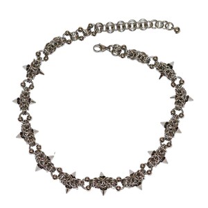 May include: Silver chainmail necklace with a series of pointed spikes. The necklace has a lobster clasp and an adjustable chain. The design incorporates intricate chainmail links and decorative elements.