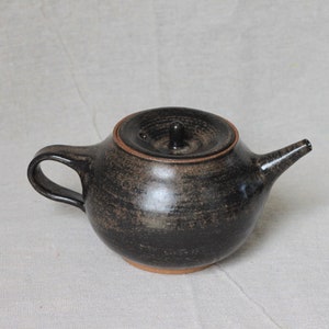 May include: A black ceramic teapot with a lid and a brown handle. The teapot has a speckled glaze and a rounded body.