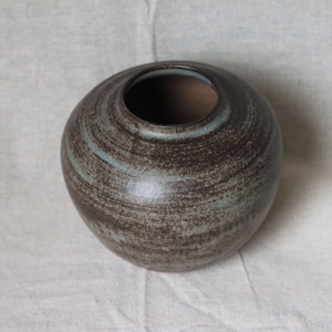 May include: A round, brown ceramic vase with a light blue glaze. The vase has a textured surface and a wide opening.