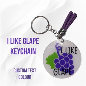 May include: A round keychain with a purple grape illustration and the text "I LIKE GLAPE". The keychain has a silver ring and a purple tassel. The text "CUSTOM TEXT COLOUR" is also visible.