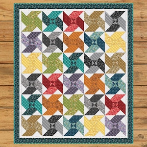 May include: A colorful quilt with a pinwheel pattern. The quilt features squares of various colors, including green, blue, red, and yellow, arranged in a grid. The quilt has a white border and a teal patterned edge.