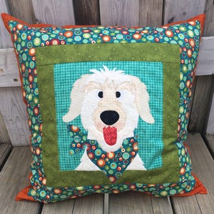 May include: Square decorative pillow featuring a whimsical dog design. The dog has white fur, a black nose, and a red tongue. The pillow has a teal background with a green border and a colorful polka dot pattern. The pillow is approximately 16 inches square.