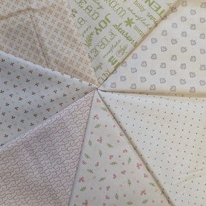 May include: A circular patchwork design composed of various fabric patterns. The fabrics feature floral, dotted, and text prints in cream, beige, and red hues. Some segments include holiday-themed text and imagery.