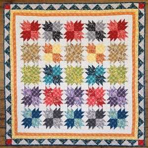 May include: A colorful quilt with a starburst pattern. The quilt features a white background with rows of star-shaped blocks in various colors, including red, blue, green, and purple. The quilt is bordered with patterned fabric and a geometric design.
