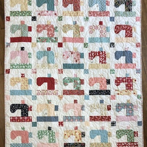 May include: A patchwork quilt with a white background and a repeating pattern of colorful sewing machines. The quilt is made up of squares of different fabrics, each with a unique design. The sewing machines are all different colors and sizes, and they are arranged in a random pattern.