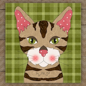 May include: A square artwork featuring a stylized cat face. The cat has brown and tan fur with dark brown stripes and green eyes. The ears are pink with white polka dots. The background is a green plaid pattern.