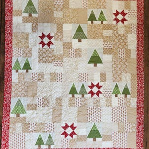 May include: A patchwork quilt featuring a repeating pattern of green Christmas trees and red starbursts on a cream and tan background. The quilt has a red floral border and is likely handmade.