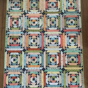 May include: A colorful patchwork quilt with a geometric design. The quilt features squares with various patterns and colors, including blue, orange, green, and pink. The quilt is bordered with a light green fabric.
