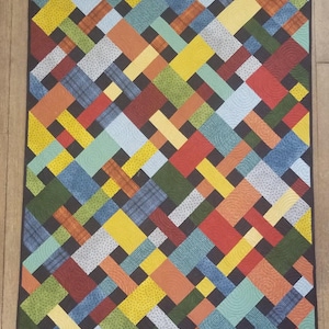 May include: A colorful quilt with a geometric pattern of squares and rectangles in shades of red, orange, yellow, green, blue, and black.