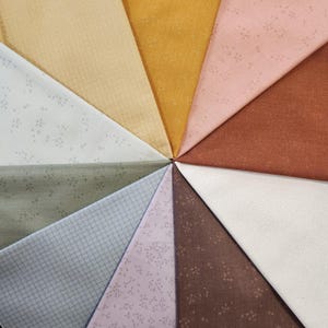May include: A collection of fabric swatches arranged in a circular pattern. The fabrics display a variety of colors, including beige, mustard yellow, pink, and brown. Some swatches have a subtle floral pattern, while others feature a grid design. The fabrics are likely cotton or linen.