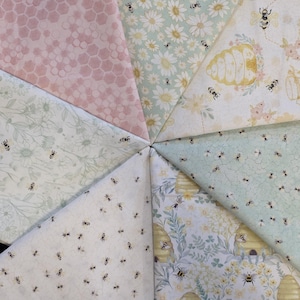May include: A collection of fabric swatches arranged in a starburst pattern. The fabrics feature various designs, including daisies, honeycombs, bees, and beehives. Colors include pink, white, and shades of green and yellow. The fabrics appear to be cotton or a similar material.