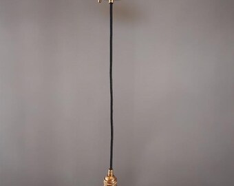 May include: A brass-colored pendant light fixture with a round ceiling plate and a black cord. The light fixture has a brass-colored bulb socket at the bottom. The fixture is suspended against a gray background.