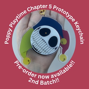 May include: A Poppy Playtime Chapter 5 Prototype Keychain. The keychain features a smiling, black and white face with a wide grin, set against a colorful jester hat design. The text "Pre-order now available!! 2nd Batch!!" is also visible.