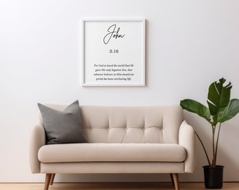 May include: A white framed print with the text "John 3:16" and the Bible verse "For God so loved the world that He gave His only begotten Son, that whoever believes in Him should not perish but have everlasting life." The print is hanging on a white wall above a light beige sofa with a gray throw pillow.