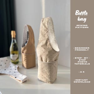 May include: Beige bottle bag with black polka dots, a pocket, and a patterned interior. The bag is designed to hold a bottle. The image also shows a bottle of wine and a sewing pattern with the text "Bottle bag".