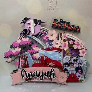 Pode incluir: Um topo de bolo em camadas com o anime Inuyasha. O design inclui o personagem Inuyasha, flores de cerejeira, o nome "Andayah" e o n&uacute;mero "1". O logotipo de Inuyasha tamb&eacute;m est&aacute; presente, com detalhes em rosa, preto e prata.