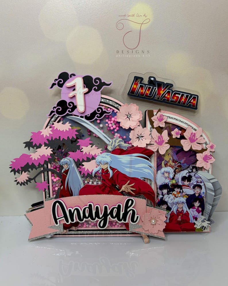Pode incluir: Um topo de bolo em camadas com o anime Inuyasha. O design inclui o personagem Inuyasha, flores de cerejeira, o nome "Andayah" e o n&uacute;mero "1". O logotipo de Inuyasha tamb&eacute;m est&aacute; presente, com detalhes em rosa, preto e prata.
