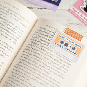 May include: Open book with a bookmark featuring a retro cassette tape design with the text "COUNTRY LOVE SONGS." Other bookmarks with whimsical designs are also visible.