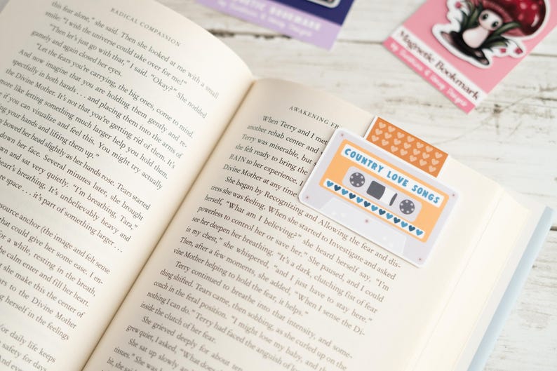 May include: Open book with a bookmark featuring a retro cassette tape design with the text "COUNTRY LOVE SONGS." Other bookmarks with whimsical designs are also visible.