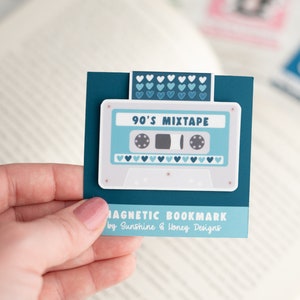 May include: A teal magnetic bookmark featuring a retro cassette tape design with the text "90's Mixtape." The bookmark has a white background with light blue accents and heart details. The text "MAGNETIC BOOKMARK" is also visible.