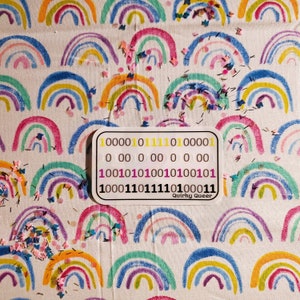 May include: A white sticker with a rainbow background and the text "Quirky Queer" at the bottom. The sticker has a series of binary code numbers in black, yellow, and pink.