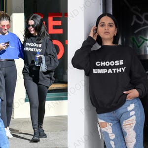 May include: Black sweatshirt with the text "CHOOSE EMPATHY" in white. The sweatshirt is worn by a person in the image. The sweatshirt is a casual style, suitable for everyday wear.