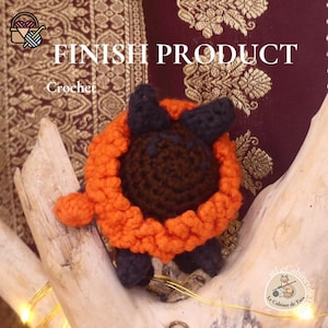 Puede incluir: Un animal de ganchillo hecho a mano con hilo naranja, marrón y negro. El texto "FINISH PRODUCT" y "Crochet" son visibles. El animal se muestra sobre un trozo de madera flotante.