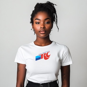 May include: A white t-shirt featuring the Royal Crown Cola logo in red, blue, and white. The logo is positioned on the front of the shirt. The model is wearing black pants.
