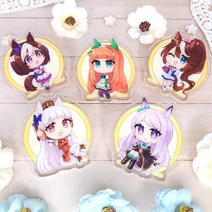 May include: Five clear acrylic charms featuring chibi-style anime characters with animal ears, each set against a circular yellow background. The characters have distinct hair colors including brown, orange, and light purple, wearing detailed outfits.