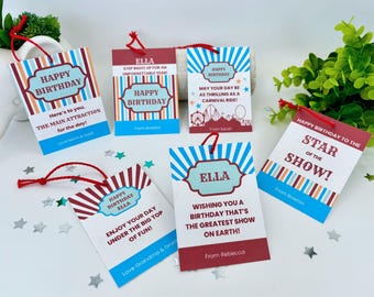 May include: A set of ten colorful gift tags with a carnival theme. The tags feature red and blue stripes, a white background, and the text "Happy Birthday" in a blue circle. The tags also include the name "Ella" and messages such as "Here's to you, the main attraction for the day!" and "Wishing you a birthday that's the greatest show on earth!"