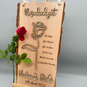 May include: A wooden sign with a laser-cut rose design and the text "Rosenhochzeit" (German for "Rose Wedding"). The sign also includes the text "Nadine & Michi" and "09. April 2025" along with the number of years, months, weeks, days, hours, and minutes in a 10-year period.