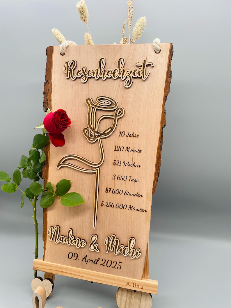 May include: A wooden sign with a laser-cut rose design and the text "Rosenhochzeit" (German for "Rose Wedding"). The sign also includes the text "Nadine & Michi" and "09. April 2025" along with the number of years, months, weeks, days, hours, and minutes in a 10-year period.