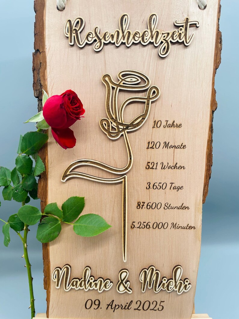 May include: A wooden sign with a carved rose design and the text "Rosenhochzeit" (German for "Rose Wedding"). The sign also includes the text "10 Jahre", "120 Monate", "521 Wochen", "3.650 Tage", "87.600 Stunden", "5.256.000 Minuten", "Nadine & Michi", and "09. April 2025".