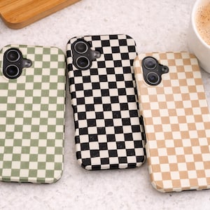 May include: Three phone cases with a checkered pattern in green, black and white, and tan and white. The cases have camera cutouts and are displayed on a light-colored surface. A cup of coffee is in the background.