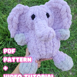 Puede incluir: Un juguete de peluche de elefante morado tejido a crochet con pies grises. El juguete está siendo sostenido por una mano. El texto "PDF PATTERN + VIDEO TUTORIAL" es visible en la imagen.