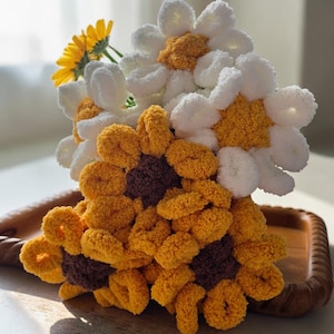 May include: A handmade bouquet of yarn flowers in a wooden tray. The flowers are white, yellow, and brown, resembling daisies and sunflowers. A single yellow flower is also included in the arrangement.