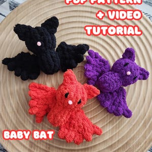 May include: Three crocheted baby bats in black, purple, and red. The bats are sitting on a wooden surface. The text "PDF PATTERN + VIDEO TUTORIAL" and "BABY BAT" are visible in the image.