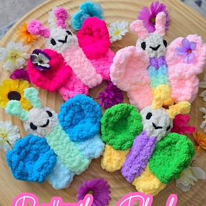 Può includere: Una collezione di giocattoli a forma di farfalla in peluche colorati con ali di vari colori, tra cui rosa, blu, verde e giallo, disposti su un vassoio di legno. L'immagine include il testo "PATTERN + VIDEO TUTORIAL" e "Butterfly Plushie".