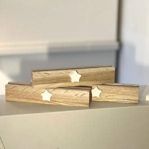 Könnte beinhalten: Drei Holz-Namensschilderhalter mit einem Stern-Ausschnitt. Die Halter sind übereinander gestapelt. Die Sterne sind weiß und das Holz ist hellbraun.