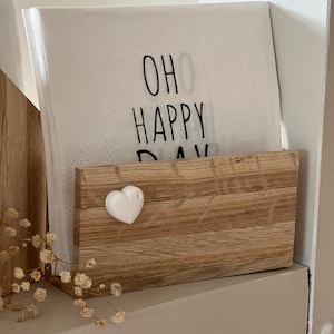 Op de afbeelding: Een houten servetthouder met een wit hart aan de voorkant. De servetthouder heeft een stapel witte servetten met de tekst "Oh Happy Day" erop gedrukt.