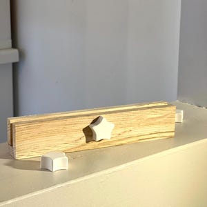 Könnte beinhalten: Ein Holzregal mit einem weißen sternförmigen Knopf. Zwei weitere weiße sternförmige Knöpfe befinden sich auf der Oberfläche unter dem Regal.