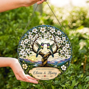 Può includere: Un acchiappasole circolare in vetro colorato con due colibrì appollaiati su un albero con fiori bianchi. Il design include uno sfondo paesaggistico e una targa in basso con il testo 40TH ANNIVERSARY, Olivia & Henry, 06.14.1986.