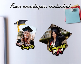 May include: Two graduation-themed magnets. One features a photo of a smiling graduate with confetti, the word "Congrats" in yellow script, and a mortarboard. The other shows a graduate in a cap and gown with a diploma and the word "Congrats". Text at the top reads "Free envelopes included".