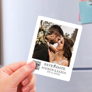 Puede incluir: Un imán rectangular blanco con esquinas redondeadas que muestra una fotografía de una pareja. El imán tiene el texto "SAVE the DATE" y los nombres "ANDREW & KAREN" con la fecha "09.12.2026". Un código QR está en la esquina inferior izquierda.