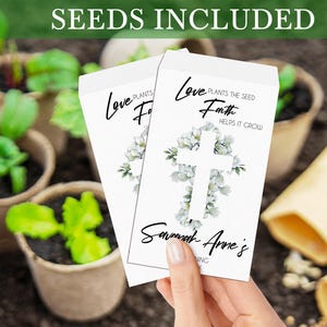 May include: White seed packet with a cross made of white flowers and the text "Love plants the seed, Faith helps it grow". The packet also has the text "Savannah Anne's" and a floral design.