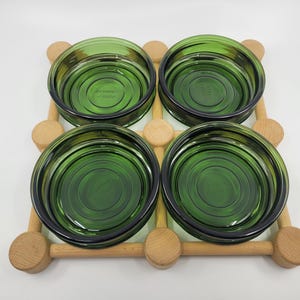 May include: Set of four green glass bowls with a wooden rack. The bowls have a ridged design and are arranged in a square pattern.