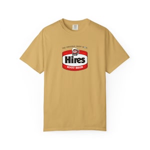 May include: A mustard yellow short-sleeve t-shirt featuring a centered graphic logo for Hires Root Beer. The logo includes the text THE ORIGINAL ROOT BEER, a small mug illustration, the word Hires in bold black, and ROOT BEER in white on red.