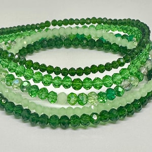 May include: A multi-strand bracelet made of green and light green glass beads. The bracelet is made of several strands of beads that are layered on top of each other.